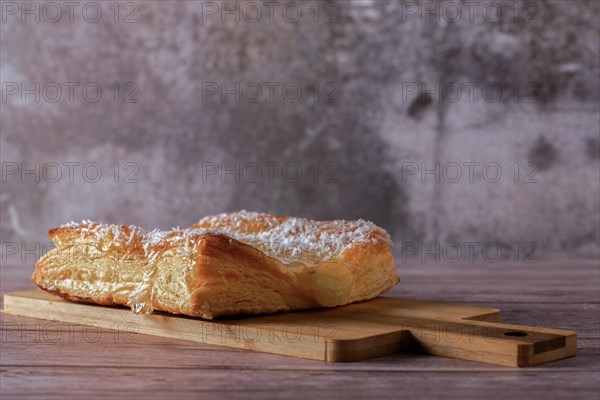 Close-up of an apple tart with shredded coconut on a wooden board with gray background and copy space