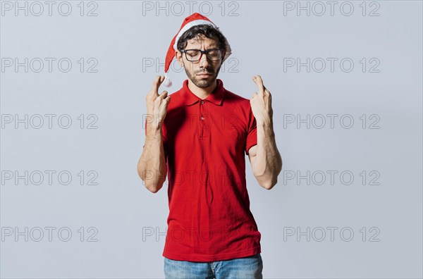 Handsome man in christmas hat making a wish on isolated background. Guy with christmas hat making a wish on isolated background