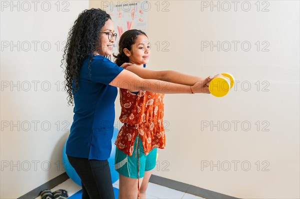 Rehabilitation physiotherapy in fitness ball. Physiotherapist helping patient with dumbbell sitting on rehabilitation ball