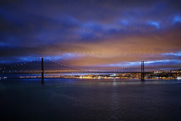 View of 25 de Abril Bridge famous tourist landmark of Lisbon connecting Lisboa and Almada on Setubal Peninsula over Tagus river in the evening twilight. Lisbon