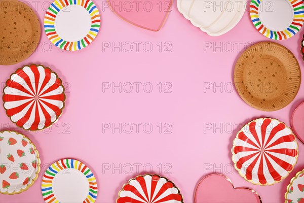 Colorful paper party plates forming border around pink background