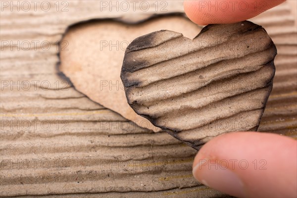 Hand holding a heart shaped burnt out of a cardboard