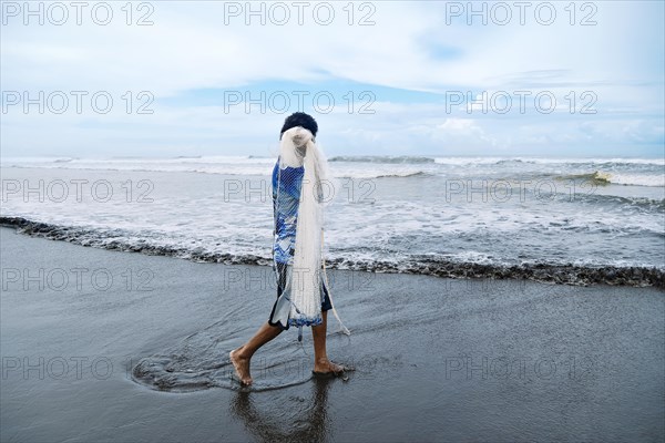 An unrecognizable fisherman walks with his net along the shore of the Pacific Sea