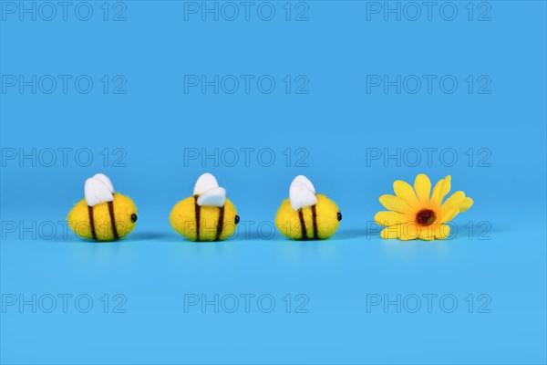 Felt bees in a row crawling towards yellow flower on blue background with copy space