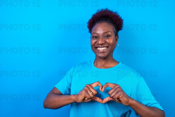 Young african american woman isolated on a blue background smiling and heart gesture