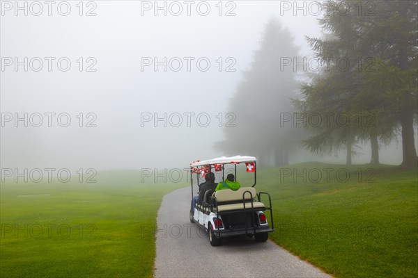 Golf cart with swiss flag on golf course with fog and trees in Crans Montana in Valais