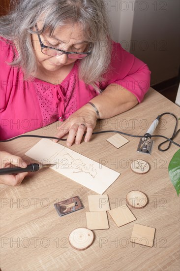 Top view of a white-haired woman drawing on a board with a pyrography pen