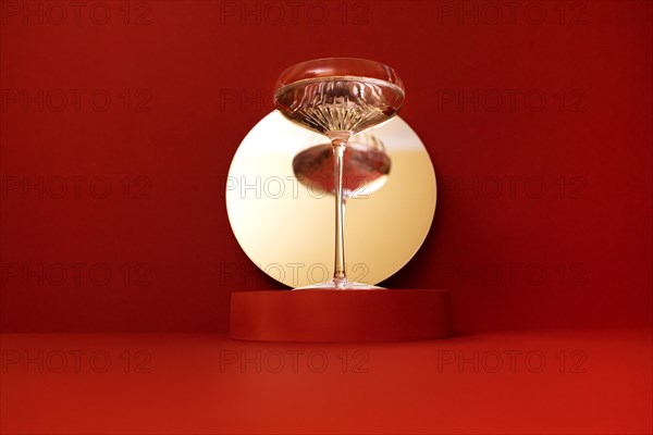 Round mirror with a stage on a bright red background. Retro glass of sparkling champagne is reflected in the mirror. Holliday concept
