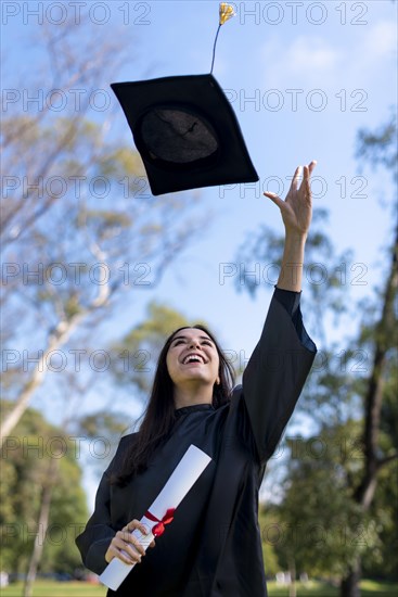 Happy caucasian graduated girl in a black gown throwing the mortarboard to the sky