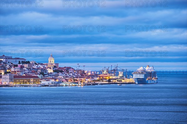 View of Lisbon over Tagus river with passing ferry boat from Almada with moored cruise liner in evening twilight. Lisbon