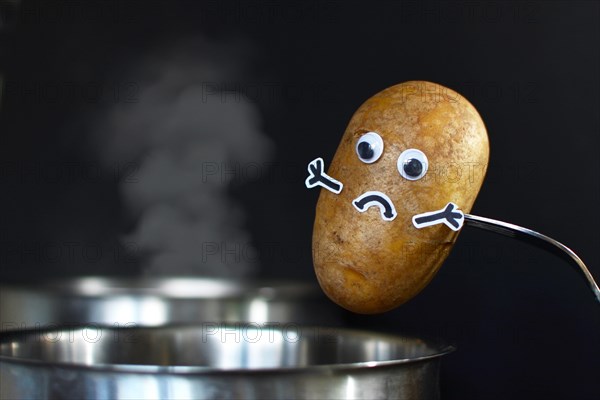 Potato with sad face and goggle eyes being put into a steaming cooking pot on dark black background