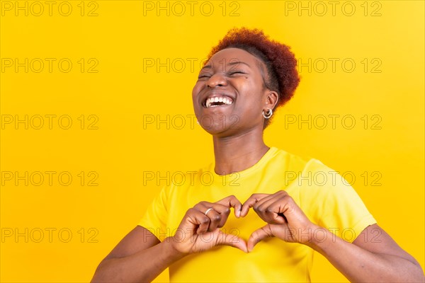 Young african american woman isolated on a yellow background smiling and heart gesture