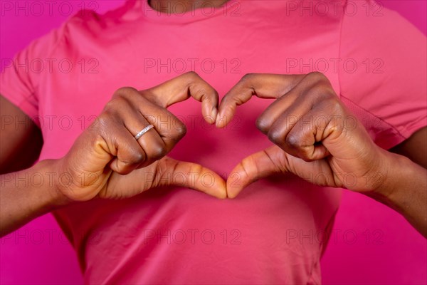 Young african american woman isolated on a pink background smiling and heart gesture