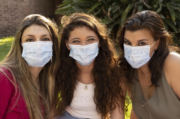 Three smiling girl friends wearing masks looking at camera