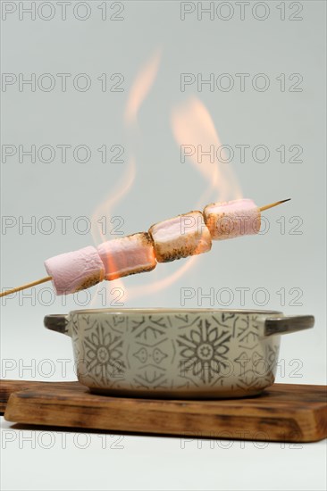 Marshmallows skewered in the fire of a ceramic bowl on a wooden board