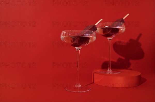 Two glasses of champagne and fruit ice cream on the podium. Stylish alcohol cocktail on red background. Delicious drinks concept. Copy space
