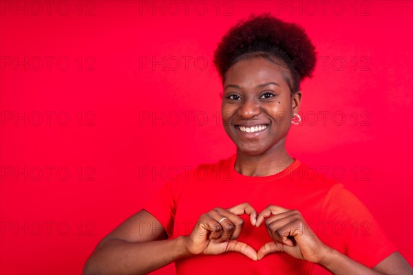 Young african american woman isolated on a red background smiling and heart gesture