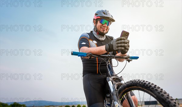 Male cyclist with helmet using cell phone. Cyclist on his bike texting with phone outdoors. cyclist man with helmet and glasses texting on cell phone outdoors