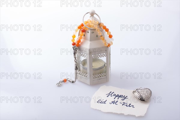 The word EID EL FITR on torn paper beside a lantern and prying beads