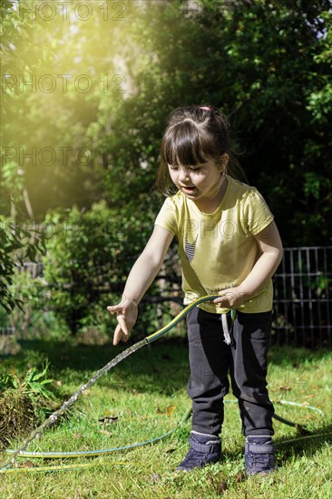 Happy little girl playing with a garden hose. Preschool child having fun with watering trees and plants in domestic garden