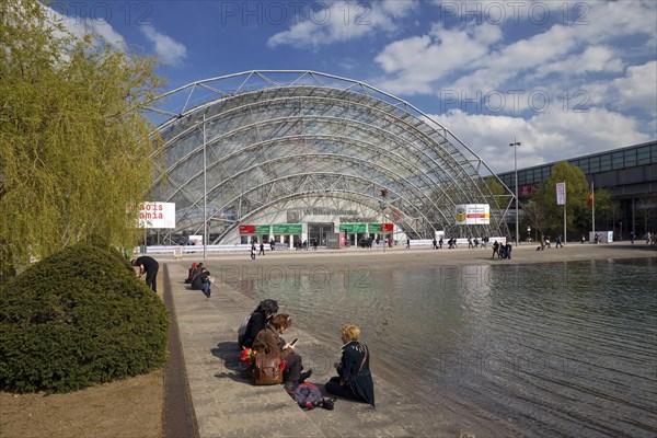 Glass hall with people at the water basin in front of the main entrance of the Leipzig Trade Fair