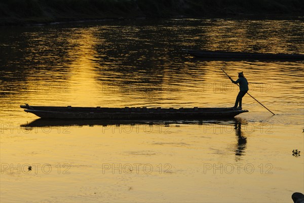 Boatman crossing the Rapti River on a traditional wooden dugout canoe. The boat is moved by pushing a long pole against the bottom of the river