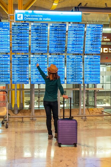 Tourist woman with suitcase at airport looking at information on screens in terminal