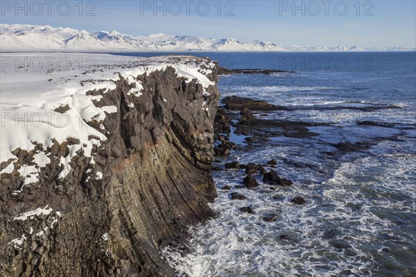 Basalt cliff in the snow in winter along the coast near Arnarstapi