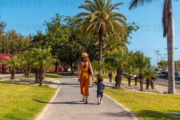 A mother with her son walking through Los Cristianos through a park with palm trees on the island of Tenerife