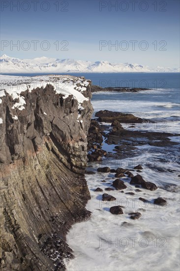 Basalt cliff in the snow in winter along the coast near Arnarstapi