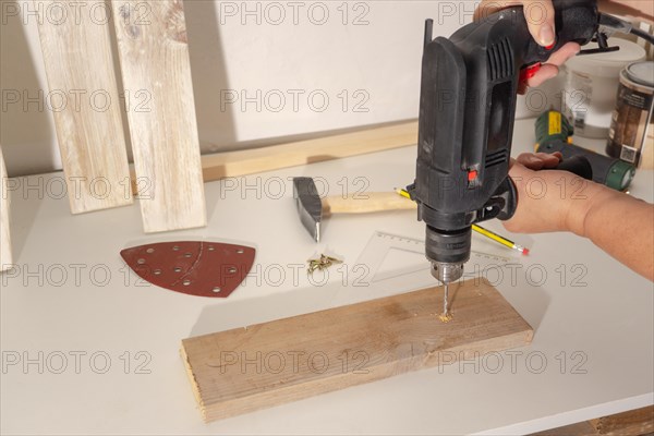 Woman's hands drilling a wooden board with an electric drill on a white board in her workshop