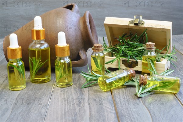 Close-up of a dropper with a drop of rosemary oil in the background several bottles of rosemary essence in a wooden box