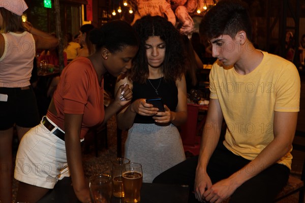 Friendly three Mixed-race chatting a phone in a bar. Concept of friendship and diversity