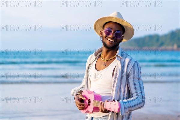 Black ethnic man enjoy summer vacation on the beach playing ukulele by the sea