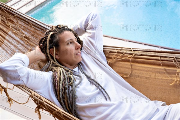 Blonde woman with dreadlocks thinking lying in a woven hammock. Resting by the pool. Holidays. Relaxing moments