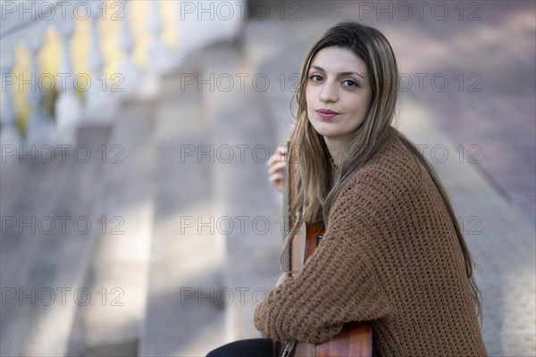 Dreamy and touched tender blonde woman plays guitar with pleased kind smile in a park