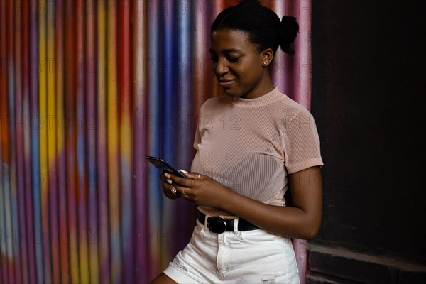 Happy black woman using smart phone and smiling on colorful background