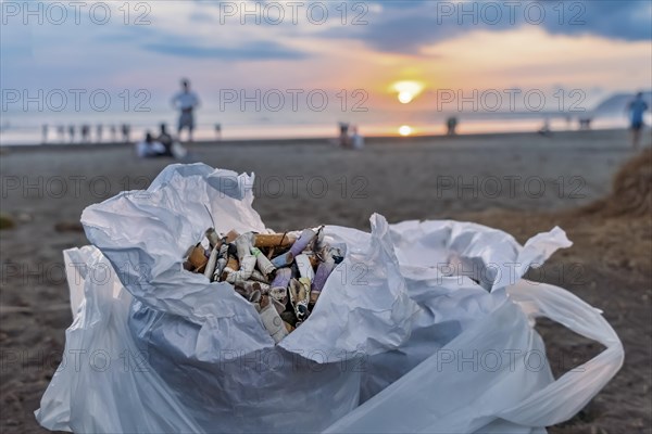 Collection of cigarette butts on the beach on the coast against the backdrop of blue sky and sea. Concept of sustainability of the planet and preservation of nature