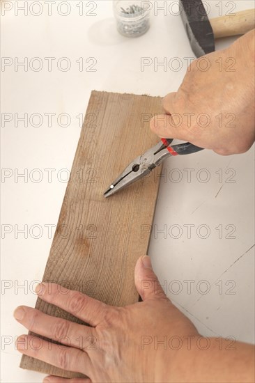 Close-up of a woman's hands pulling a nail out of a wooden board with a pair of pliers