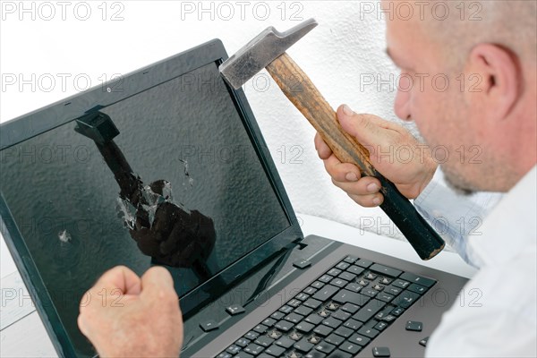 Angry man seen in profile breaking a laptop with a hammer