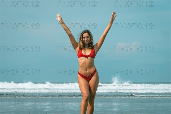 Beautiful young woman in red bikini on a turquoise water beach raising her arms