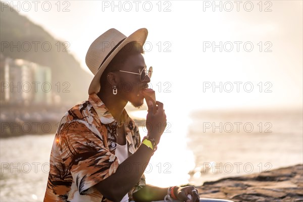 Sunset of a black ethnic man enjoy summer vacation on the beach eating an ice cream with a hat