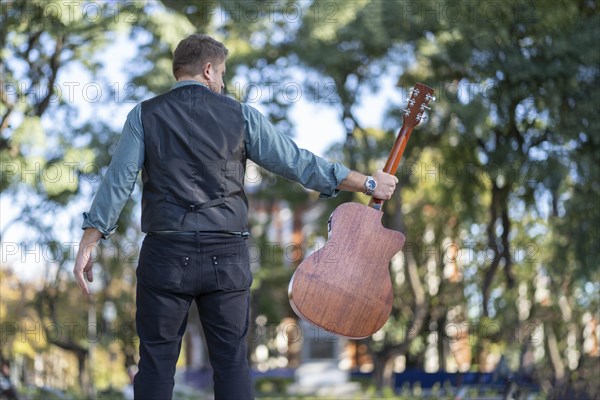 Guitarist in a park posing backwards holding his guitar with one hand