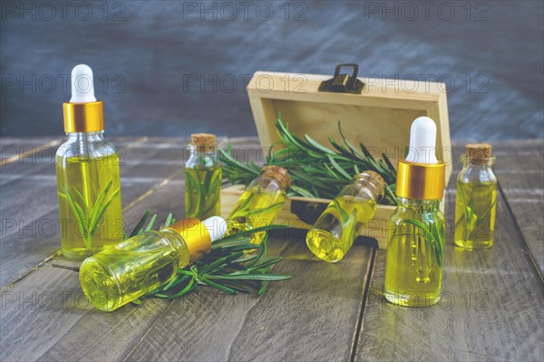 Close-up of a dropper with a drop of rosemary oil in the background several bottles of rosemary essence in a wooden box