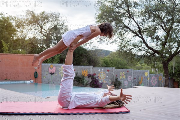 Mother balancing her daughter on her legs in the backyard of the house. Acroyoga. Mother and daughter time together. Outdoor activity. Yoga