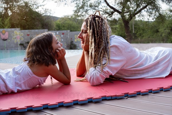 Rasta beautiful woman and a little girl lie on a mat face to face and look at each other