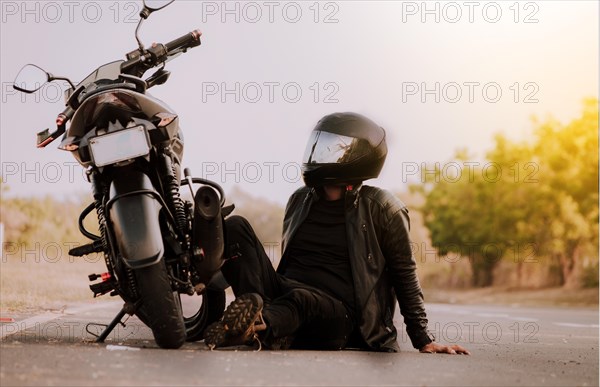 Motorcyclist sitting next to his motorcycle. Motorcyclist sitting and leaning on his motorcycle on the asphalt