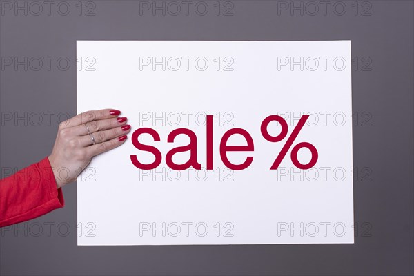 Female hand holding a SALE poster. Studio shot. Commercial concept