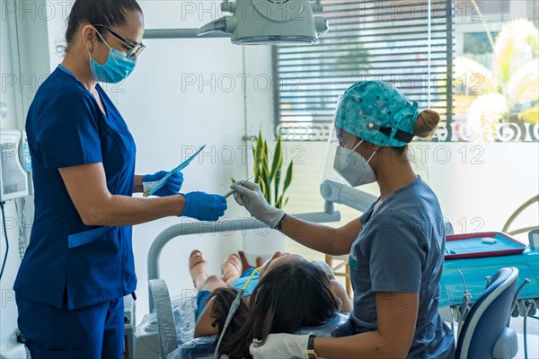 Female dentist and a female assistant in a special uniform treat the teeth of a female patient