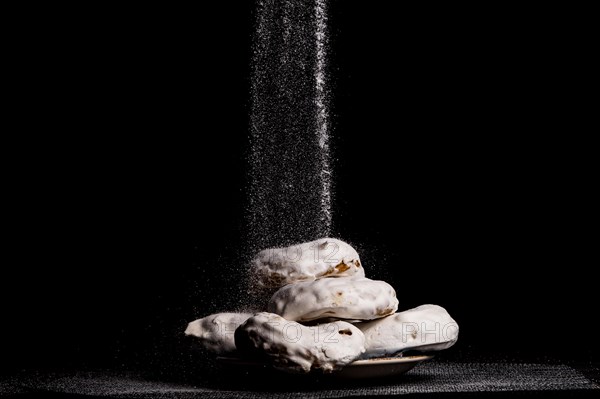 Glazed sugar doughnuts with icing sugar falling on them with black background and copy space